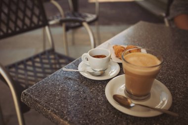 Açık bir kafedeki cam bir fincanda sütlü ve Espresso ile seçici bir odak noktası. Kahve dükkanındaki ahşap masada kahve tablosu. Bir fincan İtalyan kapuçinosu..