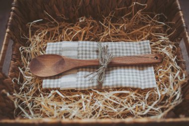 Tahta kaşık ve mutfak havlusu samanla dolu bir kutuda. Yemek pişirme konsepti. Doğal arka planda boş tahta kaşık. Mutfak ve yemek aksesuarları. Çevre dostu ürünler. Ev sahibesi için bir hediye..