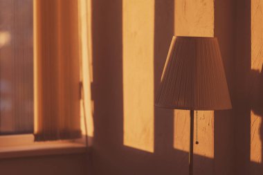 Sabah lambası ve oda duvarında güneş ışığı gölgesi. Sabah vakti sıcak bir atmosfer. Bir odanın içinde lamba, ışık ve gölge. Odada klasik lamba direği var. Duvarda asgari biçim ve gölge deseni