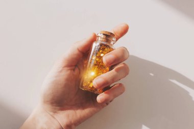 Cam kavanozda altın parıltılı bir el. Güneş ışığı altında parıldayan altın parıltısı. Beyaz masa üzerinde yıldız şeklinde parıldayan bir teneke kutu. Şişe yıldızlı süslemeler, şenlikli süslemeler.