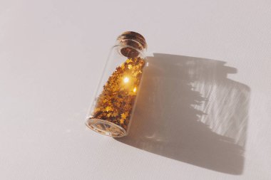 Cam kavanozda altın parıltılar. Güneş ışığı altında parıldayan altın parıltısı. Beyaz masa üzerinde yıldız şeklinde parıldayan bir teneke kutu. Altın yıldızlı bir şişe ve süs için, şenlikli süsleme..