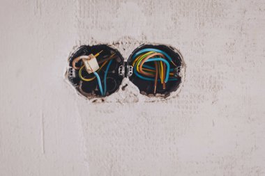 Bir oda duvarının yenilenmesi prizi ve lamba düğmesini tamir ediyor. Dairedeki elektrik kabloları tamamlanmamış elektrik prizleri elektrik kablolarıyla döşenmiş eski bir beton bina duvarı.