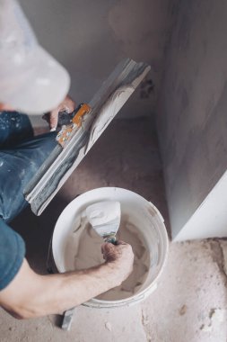 İşçi oturma odasındaki duvarları sıvamak için bir spatulaya macun koyuyor. Sıvacı iki mala sıva yapar..
