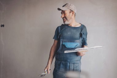Laughing Male builder, master office, plasterer with a tool in working clothes. Home improvement, spackling.  clipart