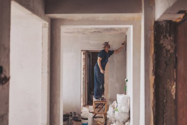 İnşaat alanında inşaat işçisi. Duvar sıvama aletleri ve apartman yenilenen işçi tulumuyla. Kapalı duvarları ve tavanları alçı ve şamandıra ile yenileyen sıva.. 