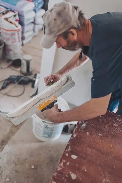 stock image Worker puts putty on a spatula for plastering internal walls in a living room. plasterer works plastering two trowels plasterboard.