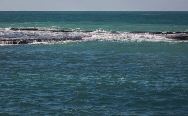 Doğa ve Manzara. Mavi deniz suyu ve kayalar. Dalgaların büyük bir kayaya çarptığı deniz manzarası