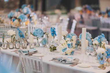 Düğün masası ayarları. Ziyafet. Sandalyeler ve masa konukları için çatal bıçak, çiçek ve mumlarla servis edilir ve masa örtüsü ve beyaz tabaklarla kaplanır.. 