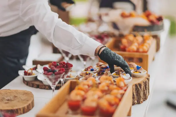 Bir garsonun elleri bir restoranda açık büfe masası için yemek hazırlar. Yemek şirketi servis masasında bir dizi aperatif hazırlıyor. Sunum ve çeşitliliğe önem veren profesyonel catering etkinliği.