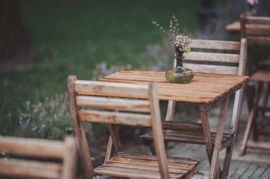 Kafe kafe restoranının terasında. Tahta sandalyeler ve parktaki çiçekli masalar. Açık teras. Sığ odaklanma. Antika sandalyeleri ve masaları olan eski moda boş kafe terası. Çatı katı tarzı kafe.