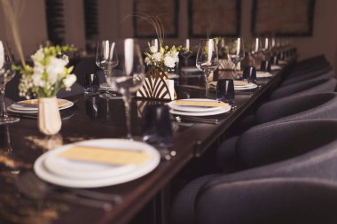 Lokantada sofra takımı çok güzel. Banquette lüks tabak ve bardaklar. Bardaklar, çatallar, bıçaklar, peçeteler ve süs çiçekleri eski, koyu kahverengi bir ahşap masa üzerinde.