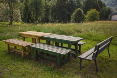 Güneş ışığında eski bir piknik tezgahı. Kırsal kesimdeki piknik tezgahları ve çalılar. Dağdaki ahşap piknik masasına yakın çekim. İtalya