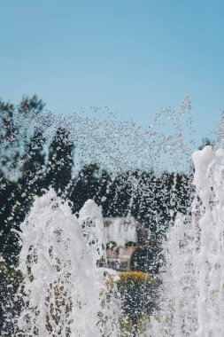 Mavi gökyüzüne karşı yakın plan su fıskiyesi. Parktaki fıskiyenin yakın çekimi. Sıcak yaz gününde şehir parkındaki çeşme. Yazın resim tazeleniyor.