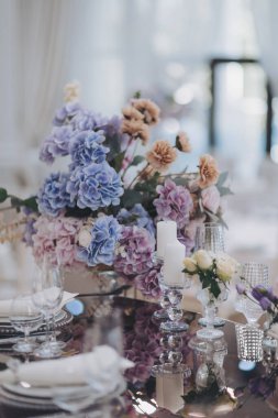 Çiçekler ve mumlar masada. Masayı mavi ve beyaz çiçekler süslüyor. Kutlama, parti ya da düğün resepsiyonu için bardaklar, tabaklar, mumlar ve çiçeklerle dolu güzel bir masa..