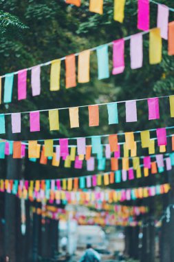 Şehir caddesinin küçük renkli bayraklarla süslenmiş görüntüleri, parkta yürüyen insanlar, şehir etkinliği için dekorasyon. Rüzgarda dalgalanan bayraklar. Şehir arka planında dekoratif çok renkli bayraklar