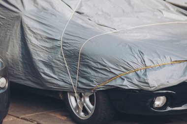 Koruyucu giysi altında park edilmiş bir araba. araba kılıfı, gümüş araç çadırı, güneş koruması, kötü hava koşulları araba koruması.