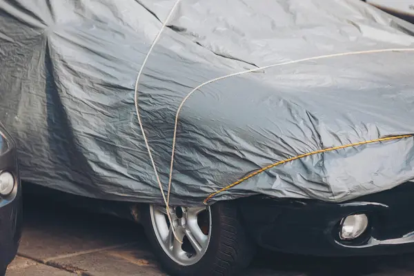 Koruyucu giysi altında park edilmiş bir araba. araba kılıfı, gümüş araç çadırı, güneş koruması, kötü hava koşulları araba koruması.