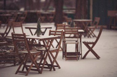 Masası, sandalyeleri ve Noel süslemeleri olan bir Noel terası. Karlı bir kış sokağı sahnesi. Ahşap masası, sandalyeleri ve dekoratif küçük çam ağacı olan bir Noel kafesi. Yeni yıl konsepti