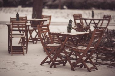 Masası, sandalyeleri ve Noel süslemeleri olan bir Noel terası. Karlı bir kış sokağı sahnesi. Ahşap masası, sandalyeleri ve dekoratif küçük çam ağacı olan bir Noel kafesi. Yeni yıl konsepti