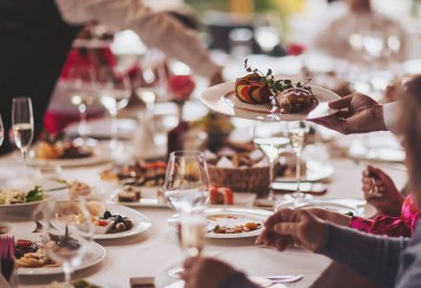 İnsanlar bir restoranda öğle veya akşam yemeği yiyorlar. Tabaklar masaya. Garson, şenlikli bir etkinlikte et tabağı taşıyor..
