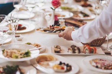 Garson festival masasını hazırlar. Tabaklar masaya. Restoranda servis yapan garson misafirleri ağırlamaya hazırlanıyor. Garson, şenlikli bir etkinlikte et tabağı taşıyor..