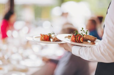 Garson festival masasını hazırlar. Tabaklar masaya. Restoranda servis yapan garson misafirleri ağırlamaya hazırlanıyor. Garson, şenlikli bir etkinlikte et tabağı taşıyor..