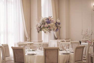 Şenlikli düğün dekorasyonu. Düğün günü yemek masasında cam vazoda güzel taze çiçekler. Çiçekli lüks düğün dekoru ve yuvarlak masalarda mücevherleri olan cam vazolar. Pahalı yemekler.