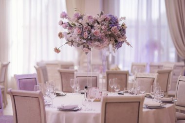 Şenlikli düğün dekorasyonu. Düğün günü yemek masasında cam vazoda güzel taze çiçekler. Çiçekli lüks düğün dekoru ve yuvarlak masalarda mücevherleri olan cam vazolar. Pahalı yemekler.