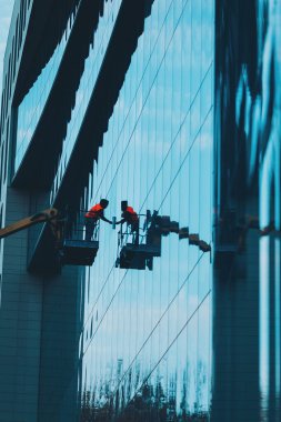 Modern binaların cam temizleyicisi, asansör platformunda havada asılı duran erkek. Havada çalışan camlar var. Bir işçi vinç platformundan bir binanın camlarını siler.