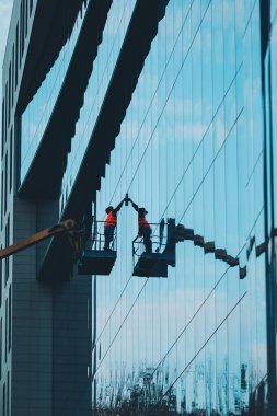 Modern binaların cam temizleyicisi, asansör platformunda havada asılı duran erkek. Havada çalışan camlar var. Bir işçi vinç platformundan bir binanın camlarını siler.