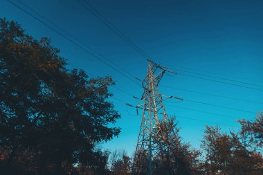 Yüksek voltajlı bir güç iletim hattı, fotoğrafta, mavi gökyüzüne karşı bir güç hattı desteği. Güneş ışığında mavi gökyüzünün arka planında yüksek voltaj kabloları olan direkler. Güç hatları grubu.
