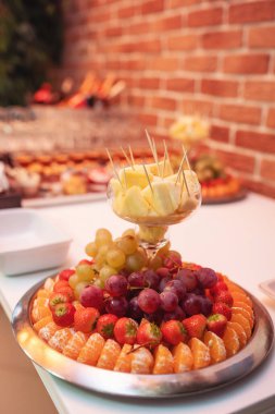 Yemek masasında lezzetli düğün tatlıları. Farklı meyveli bir tabak. Portakal, üzüm, ananas, çilek ve böğürtlenli lüks düğün büfesi..