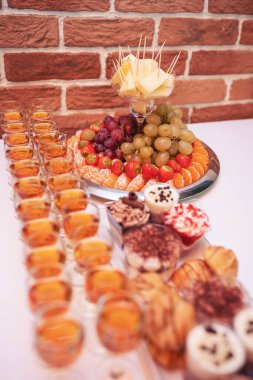 Yemek masasında lezzetli düğün tatlıları. Farklı meyveli bir tabak. Portakal, üzüm, ananas, çilek ve böğürtlenli lüks düğün büfesi..