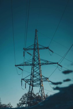 Gün batımında arka planda berrak, berrak bir gökyüzü olan bir su kütlesinin yansımaları. Gökyüzüne karşı elektrik direğinin düşük açılı görüntüsü