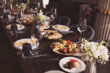 Restoran salonundaki parlak ve şenlikli masa. Lokantada masa ayarlandı. Arkadaşların ev partisi için farklı lezzetli yemeklerle kahvaltı masası hazırlamak. Masada çeşitli yiyecekler var.