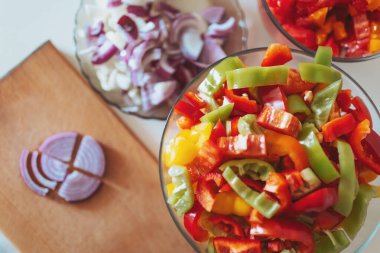 Pişirilmeye ya da kızartılmaya hazır sebzeleri kes. Kesme tahtasında kesilmiş sebzeler. Doğranmış dolmalık biber, domates ve soğan. Üst görünüm.