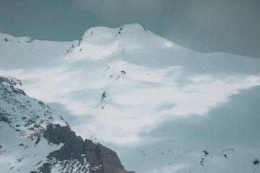 Işık ve gölgeli karların altındaki yüksek dağlar. Dağ zirvesi ve sisli gökyüzü