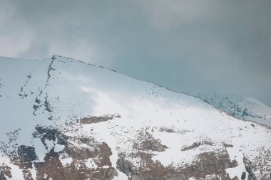 Işık ve gölgeli karların altındaki yüksek dağlar. Dağ zirvesi ve sisli gökyüzü