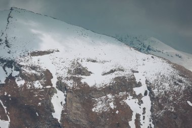 Işık ve gölgeli karların altındaki yüksek dağlar. Dağ zirvesi ve sisli gökyüzü