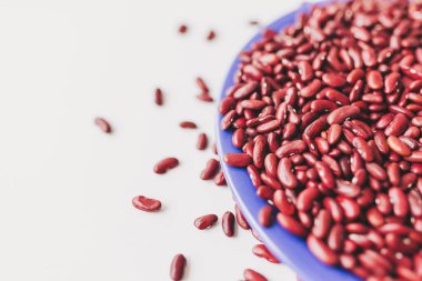 Vibrant red kidney beans spill from a blue plate, showcasing a rich harvest in a bright kitchen setting clipart