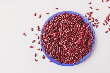 Kırmızı böbrek çekirdekleri canlı mavi bir tabakta güzel bir şekilde düzenlenmiş, temiz beyaz arka planda zengin renklerini ve doğal dokularını sergiliyorlar.