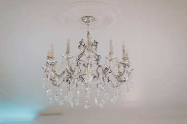 Elegant crystal chandelier illuminates a lavish room with ornate decor and soft glowing light during an evening gathering clipart