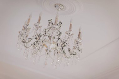 Elegant crystal chandelier illuminates a lavish room with ornate decor and soft glowing light during an evening gathering clipart