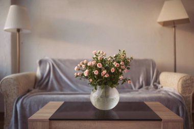 Sıcak ışıklandırması ve yumuşak mobilyaları olan rahat bir oturma odasında, sehpanın üzerinde güzel bir buket çiçek.