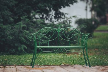 Çekici, yeşil, ıslak bir bank, taştan bir patikada dinleniyor. Ziyaretçiler sakin bir günde sakin bir bahçenin huzurlu ortamının tadını çıkarıyorlar.