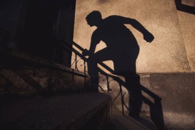 Bir bireyin gölgesi binanın dışındaki merdivenlerden yükseliyor. Güneş ışığı dokulu duvara çarpıcı bir siluet fırlatıyor ve dramatik bir etki yaratıyor. Hırsızlık konsepti Korku. fobi.
