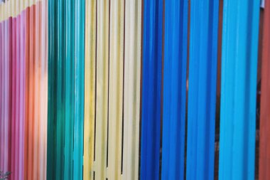 Çeşitli parlak renklerdeki dikey metalik levhalar ışık ve yaratıcılık hissiyle dolu açık havada neşeli bir zemin oluşturur. Düzenleme eğlenceli bir estetik sunuyor.