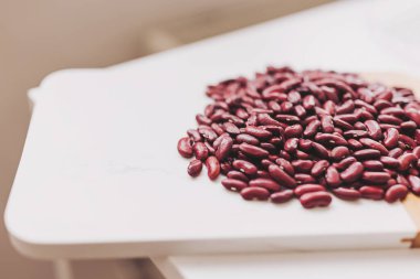 Canlı kırmızı fasulye koleksiyonu ahşap bir kesme tahtasına saçılmış, çeşitli yemek ve yemekler için zengin renklerini ve besin faydalarını vurguluyor.