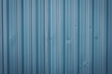 Duvardaki metal levha. Mavi kıvrımlı metal duvar, hava kararırken soğuk bir endüstriyel ortamda ince desen ve ince kusurlar sergiliyor.