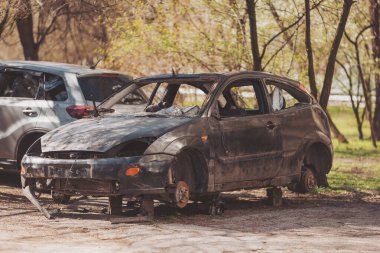 Terk edilmiş araç, ağaçlar ve doğanın cazibesiyle çevrili sessiz bir parkta, bahar güneşinin erken saatlerinde dinleniyor. Mahvolmuş araç sokakta. Trafik kazası kavramı..